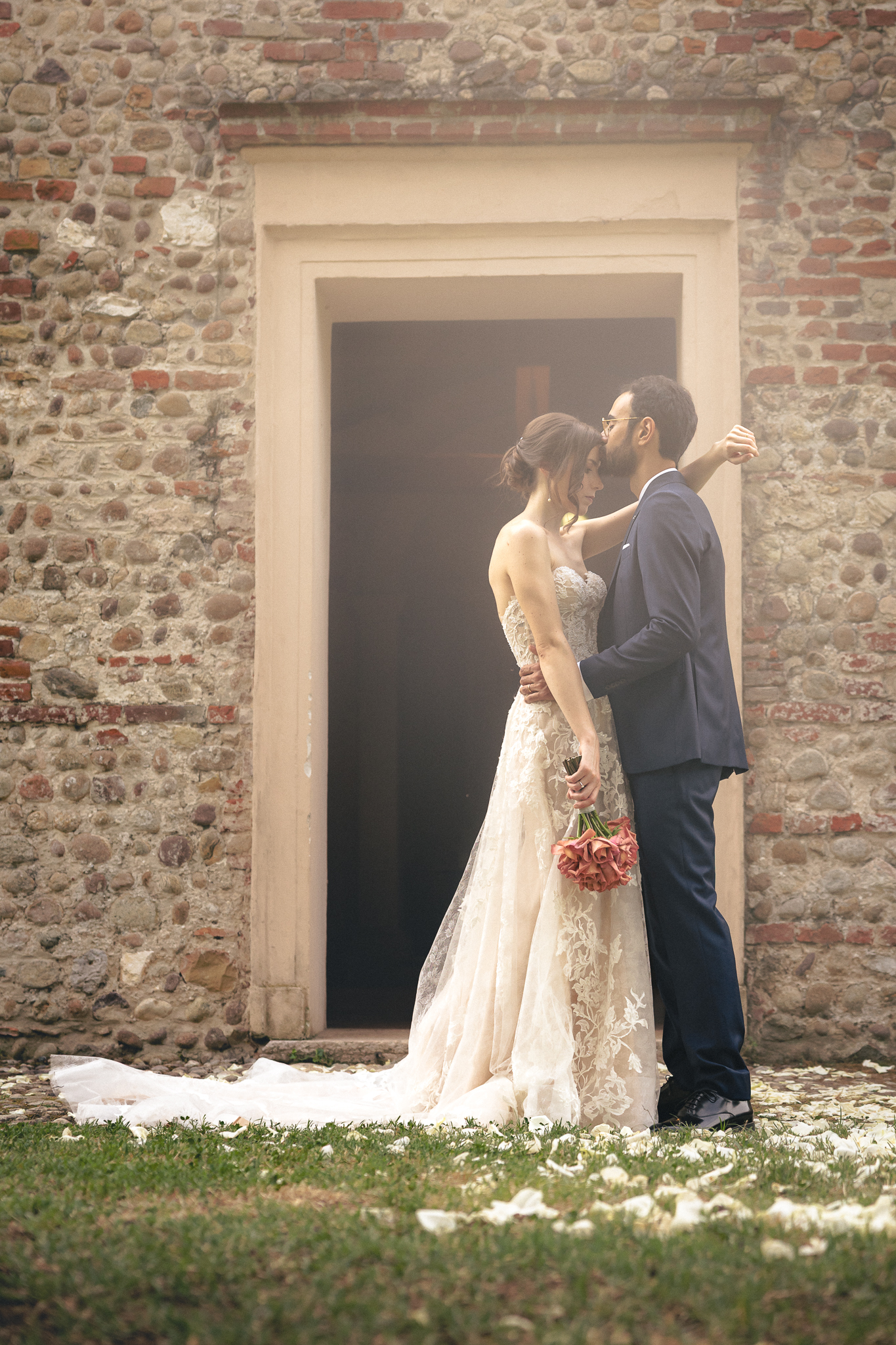 Gli sposi con il bouquet di rose rosse davanti alla porta dell’oratorio