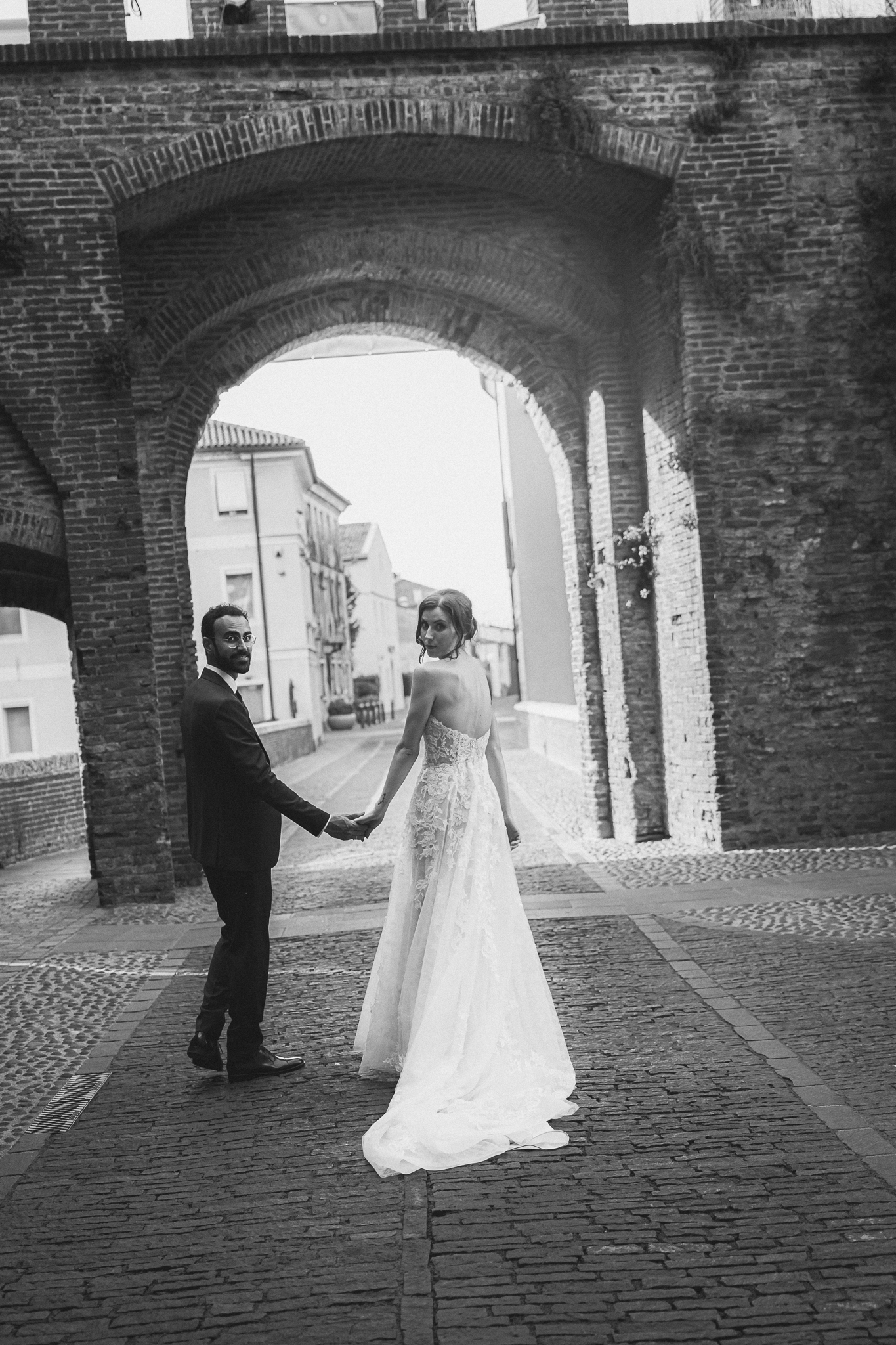 Gli sposi passeggiano sotto un arco in mattoni, in bianco e nero
