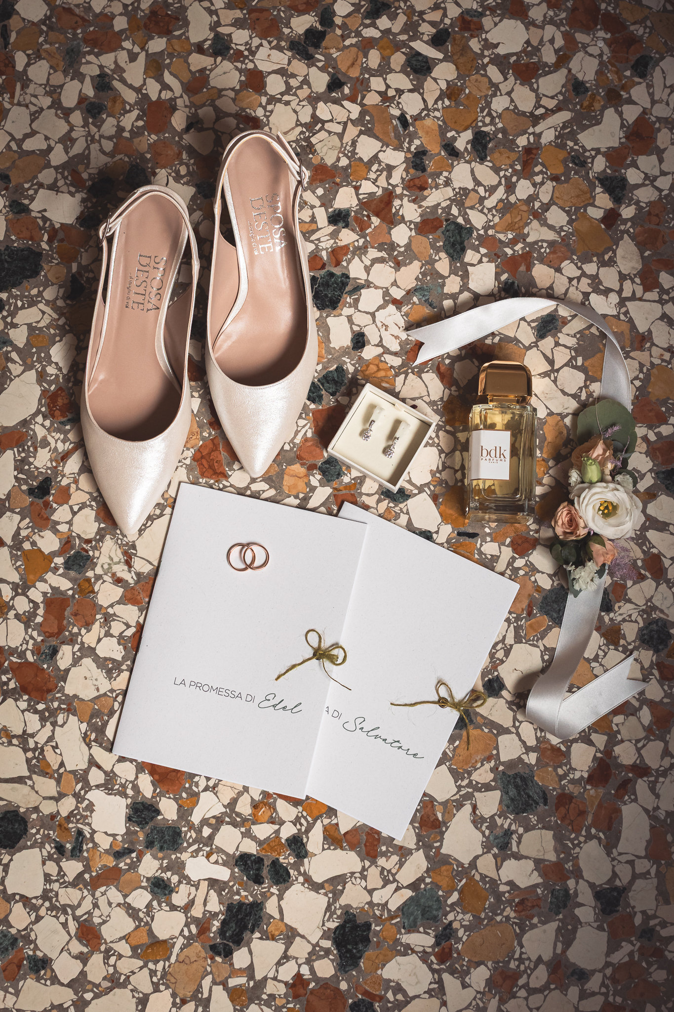 Le scarpe da sposa, l'invito e le fedi appoggiati sul pavimento a terrazzo veneziano