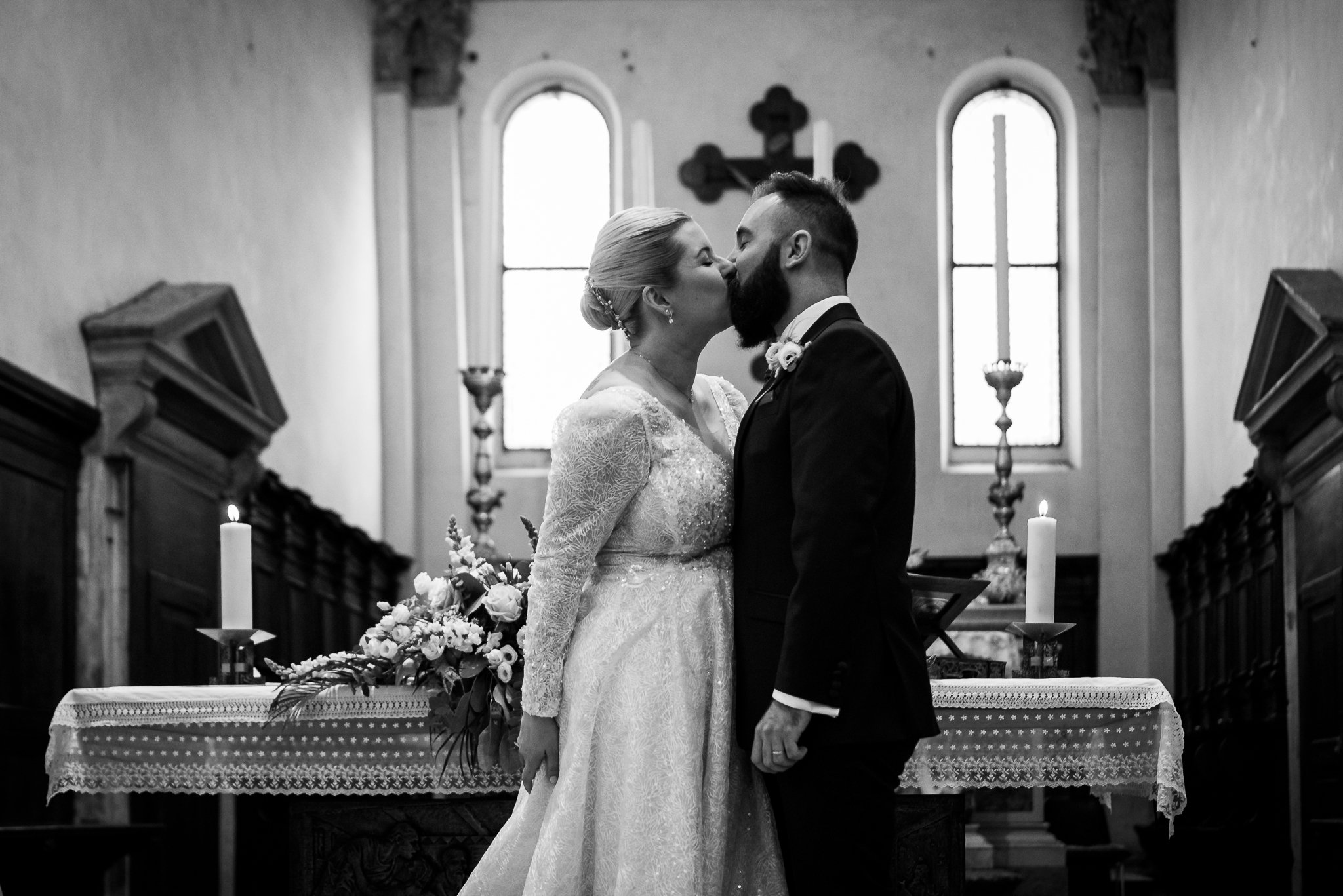 Il bacio degli sposi in bianco e nero, tra le finestre ad arco della chiesa