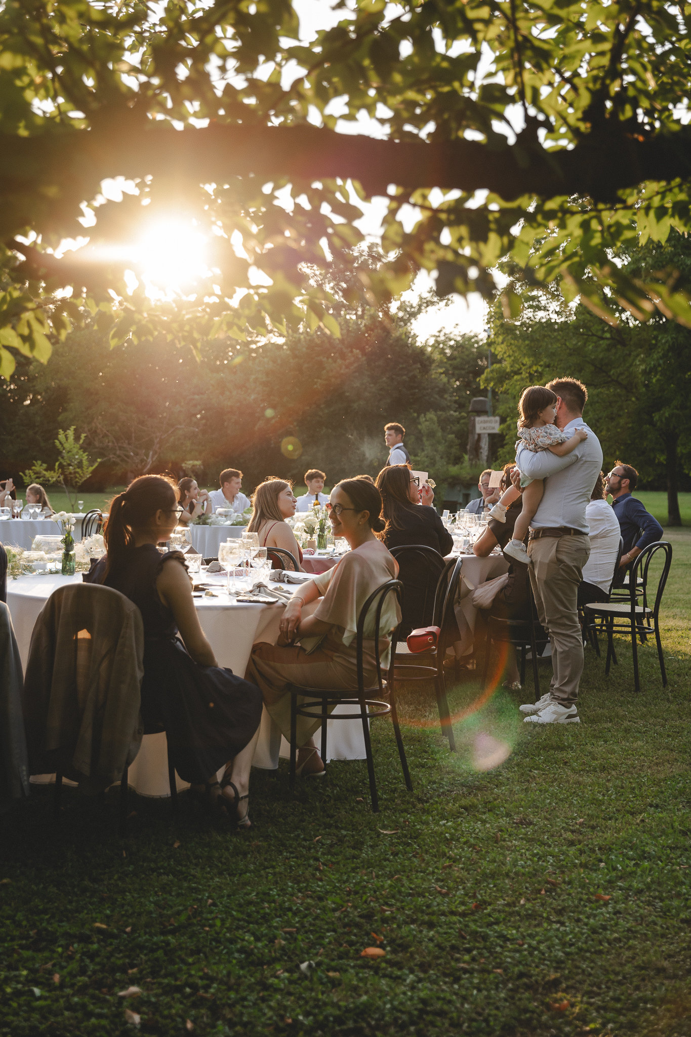 Gli invitati a tavola con il sole che filtra tra gli alberi